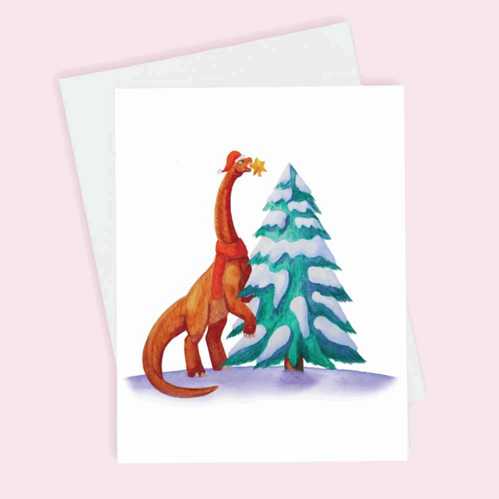 A holiday greeting card depicting an orange brachiosaurus wearing a red scarf and matching holiday hat placing a star on top of a frosted Christmas tree done in watercolor.