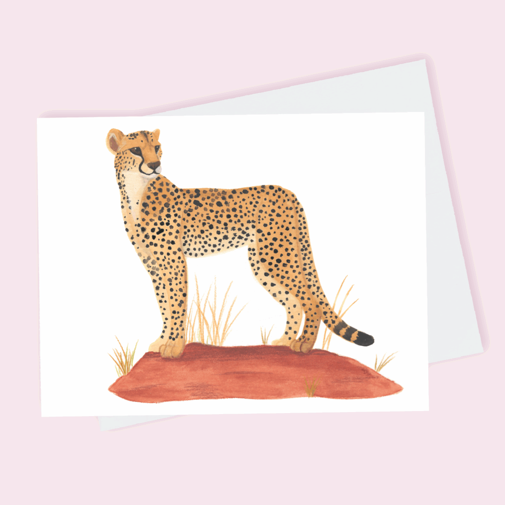 A greeting card depicting a cheetah in traditional yellow with black spots standing atop an earthy red hill done in watercolor.
